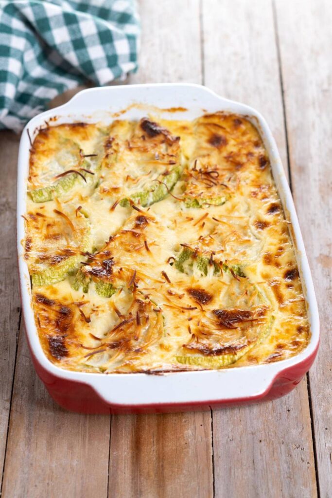 Kessel mit Käse und Gratin-Zucchini auf einem Holztisch